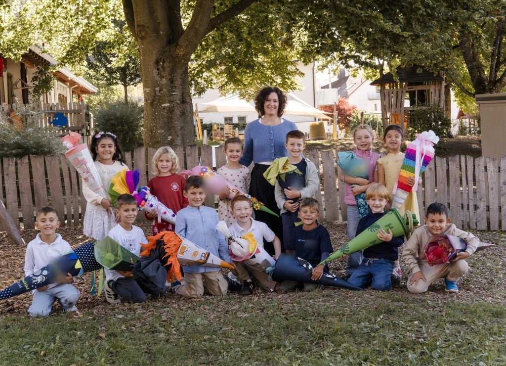 Klassenfoto der Klasse 1 (Drachenklasse) mit Klassenlehrerin Frau Tanja Felix-Lademann vor einem Holzzaun auf dem Schulhof, die Kinder mit ihren Schultüten