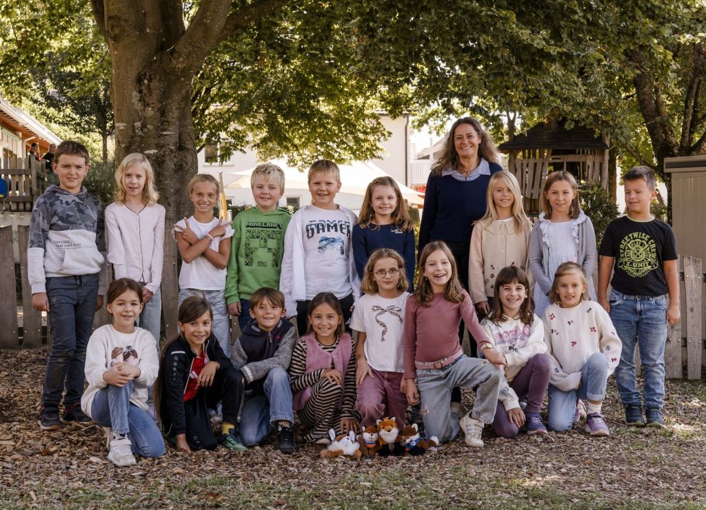 Klassenfoto der Klasse 3 (Fuchsklasse) mit Klassenlehrerin Frau Rabea Lähndorff-Schorr unter einem großen Baum auf dem Schulhof, vorne liegen Stofffüchse
