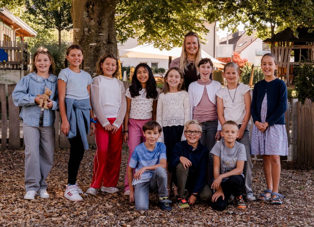 Klassenfoto der Klasse 4 (Bärenklasse) mit Lehrerin Frau Nicole Mack unter einem großen Baum auf dem Schulhof, vorne knien drei Jungen, ein Mädchen hält einen kleinen Stoffbären